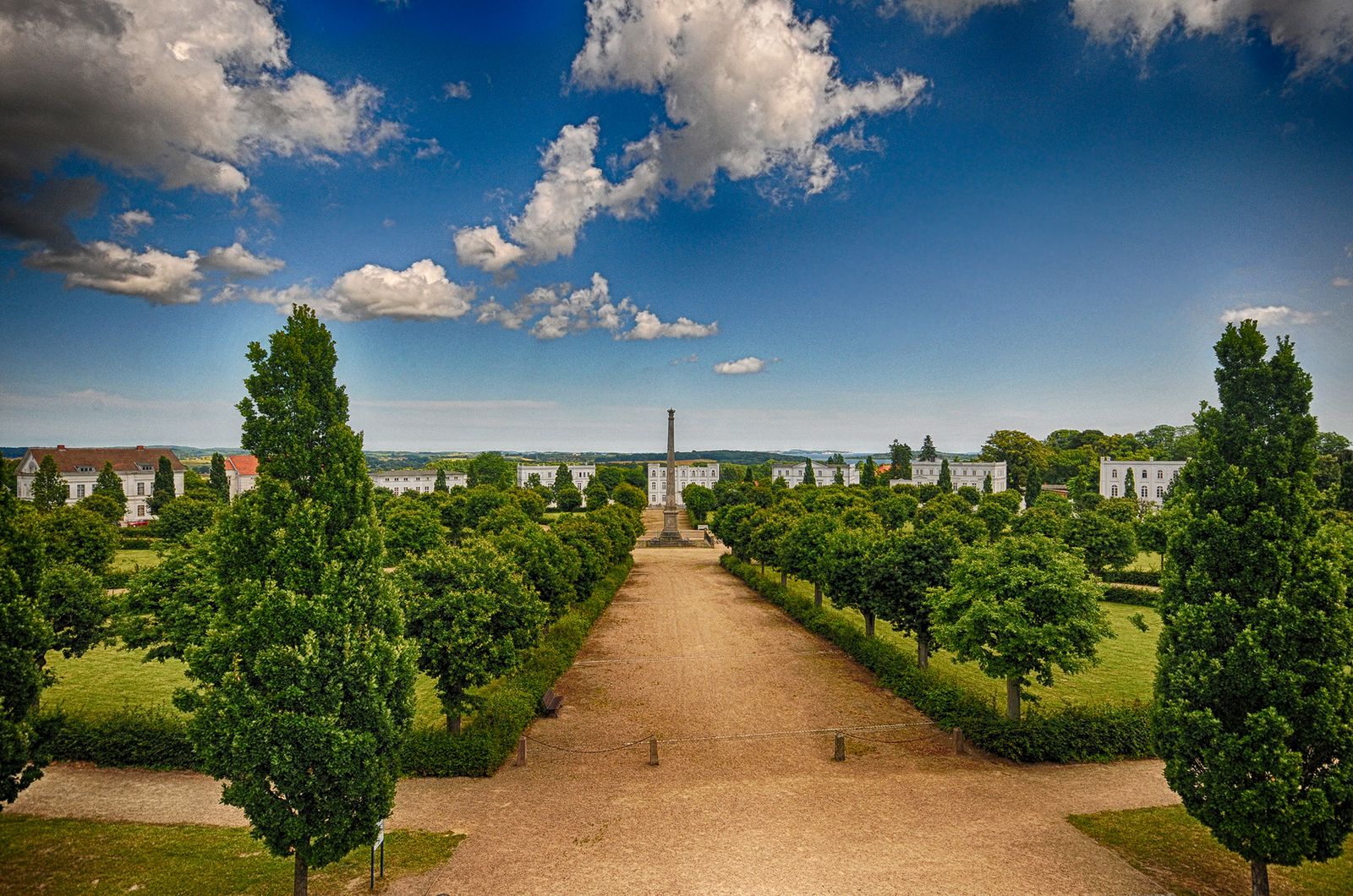 Der Circus in Putbus mit Obelisk, Lindenallee und weißen klassizistischen Häusern unter blauem Himmel